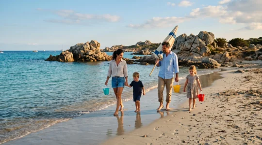 Une famille avec deux enfants marche le long d'une plage corse aux eaux calmes.